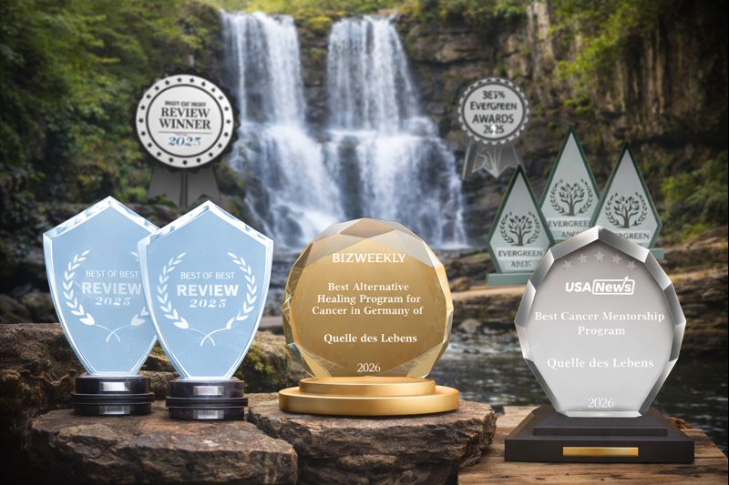 Eine Sammlung von Auszeichnungen steht in der Nähe eines Wasserfalls. Zu sehen sind mehrere Trophäen, darunter Auszeichnungen für "Best Alternative Healing Program for Cancer in Germany" und "Best Cancer Mentorship Program."